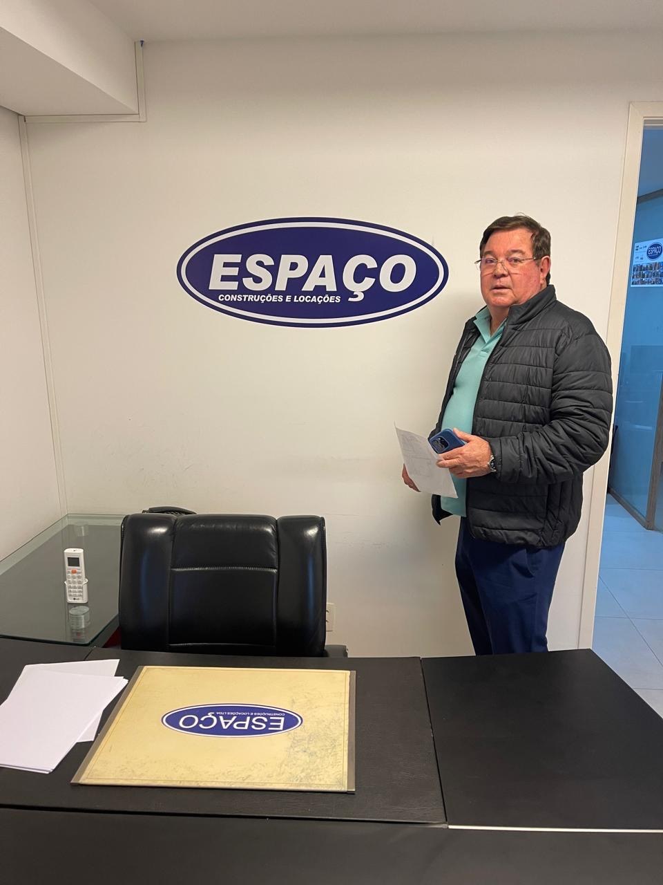 Representante da Espaço Construções em ambiente institucional ao lado da marca da empresa